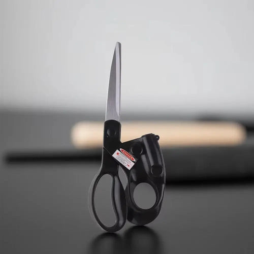 Black-handled scissors on a reflective surface with a blurred background